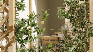 A wooden chair and table set in a sunlit room with a wooden lattice structure and green foliage. - Hydria Residence (Matera)