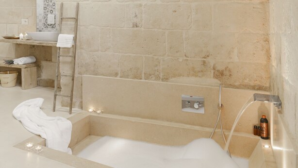 A modern bathroom with a stone wall, a bathtub, and a shower area. - Hydria Residence (Matera)