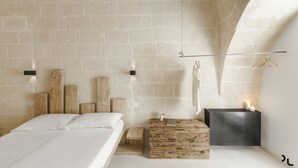 A bedroom with a brick wall, wooden headboard, a bedside table with a book, and a hanging light fixture. - Hydria Residence (Matera)