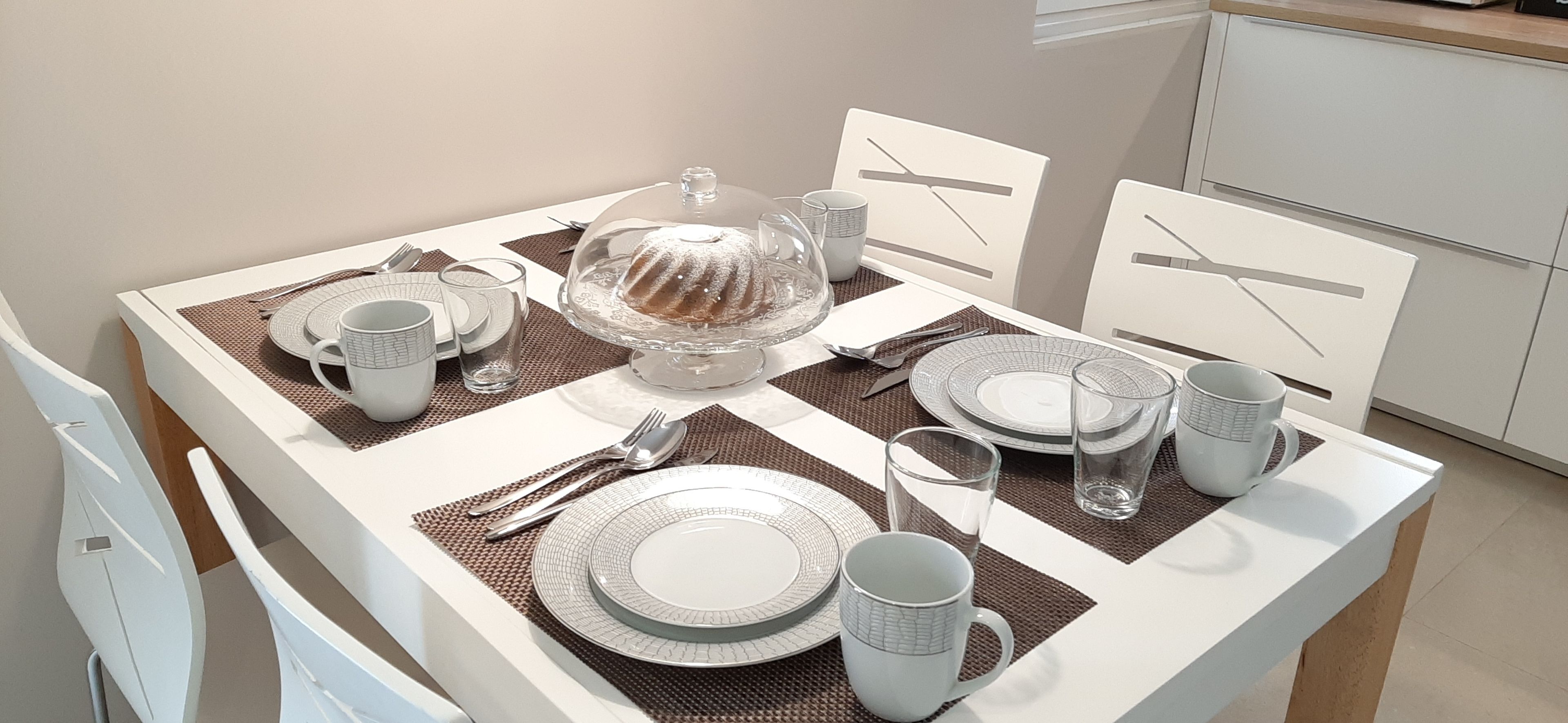Une table à manger dressée avec des assiettes, des couverts et un gâteau en forme de couronne, le tout posé sur un set de table.