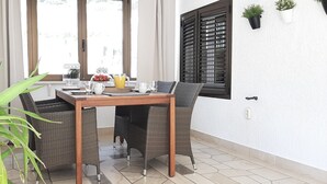 Ein Essbereich mit Tisch und Stühlen, einer Zimmerpflanze und einem Fenster mit Fensterläden.