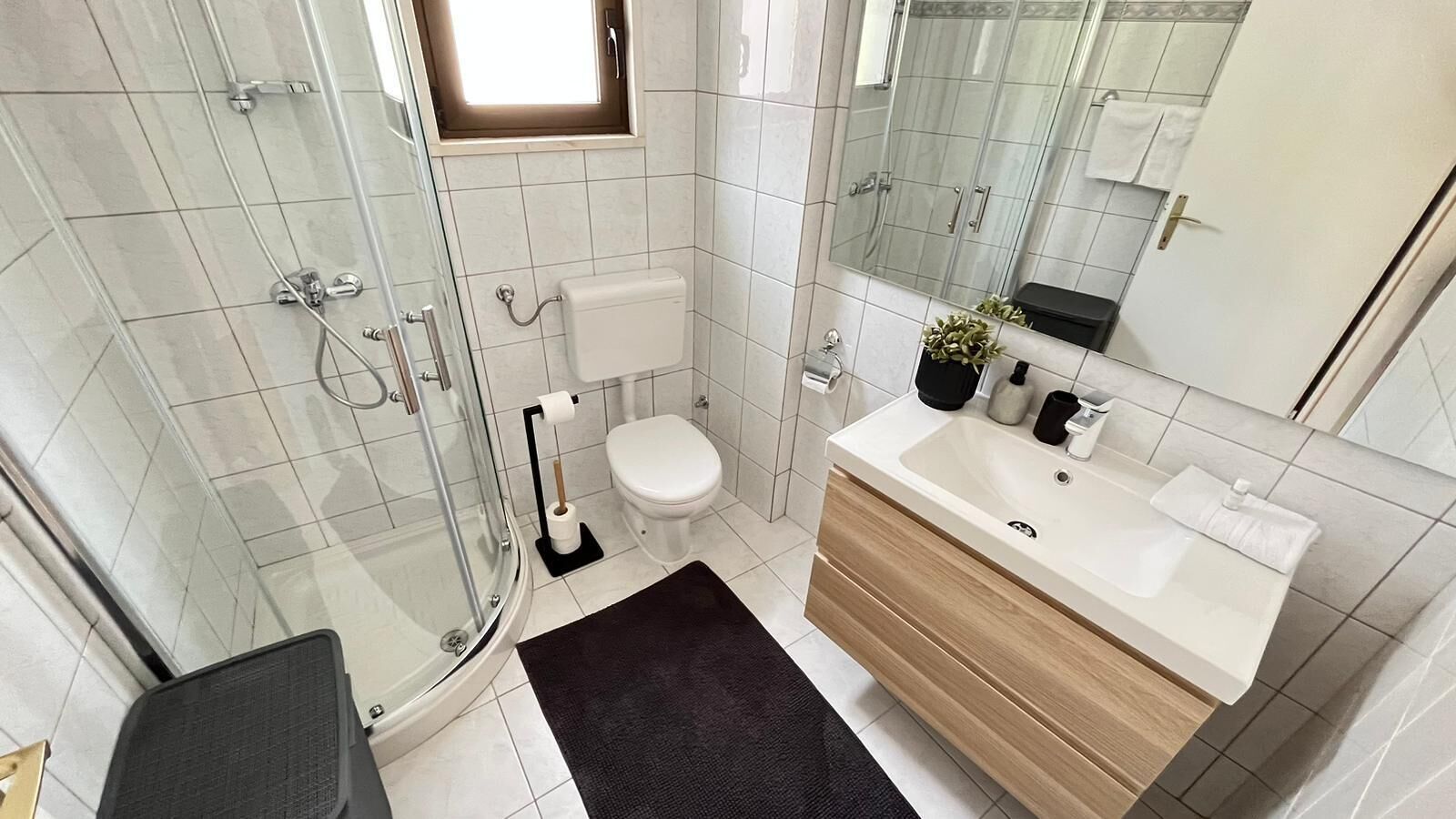Une salle de bain moderne dotée d’une douche à parois de verre, de toilettes et d’un meuble-lavabo avec un évier et un miroir.