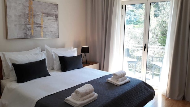 Ein Hotelzimmer mit einem großen Bett, zwei Kissen, einer schwarzen Bettdecke und Blick ins Freie durch eine Schiebetür.