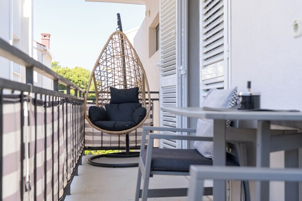 A balcony with a hanging chair, a table with a chair, and a small table with a bottle. - Guesthouse Civljak (Baska Voda)