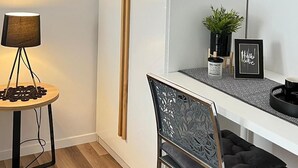 Ein modernes Zimmer mit einem weißen Kleiderschrank, einem kleinen runden Tisch mit Lampe, einem Stuhl und einer Topfpflanze.