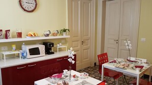 A dining area with a table set for two, a microwave, a coffee maker, and a clock on the wall. - Central Suites (Catania)