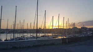 A marina with multiple sailboats docked, a waterfront view, and buildings in the background. - Central Suites (Catania)