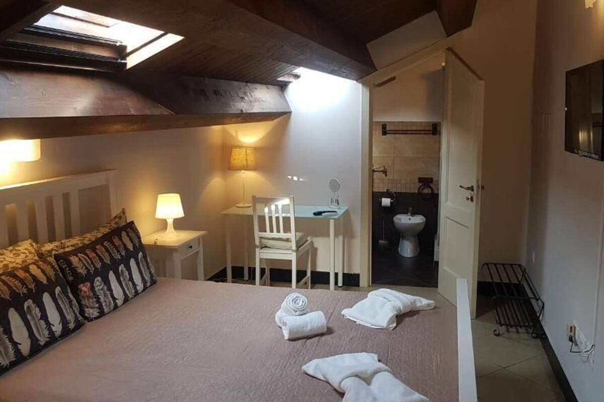 A bedroom with a bed, bedside table, lamp, chair, and towels.