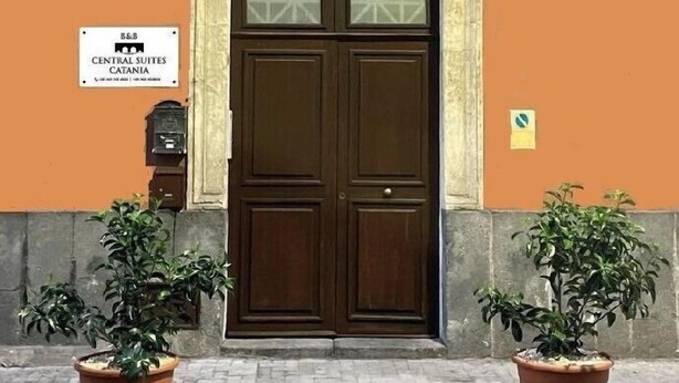A central suites catania sign, a brown double door with glass panels, and two potted plants on the pavement. - Central Suites (Catania)