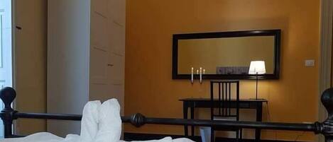 A hotel room with a bed, a bedside table with a lamp, a mirror on the wall, and a wardrobe.