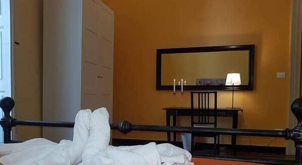 Una camera d'albergo con un letto, un comodino con una lampada, uno specchio a parete e un armadio.