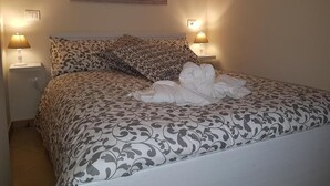 A neatly made bed with patterned bedding, two bedside lamps, and a wall-mounted artwork above the bed. - Central Suites (Catania)