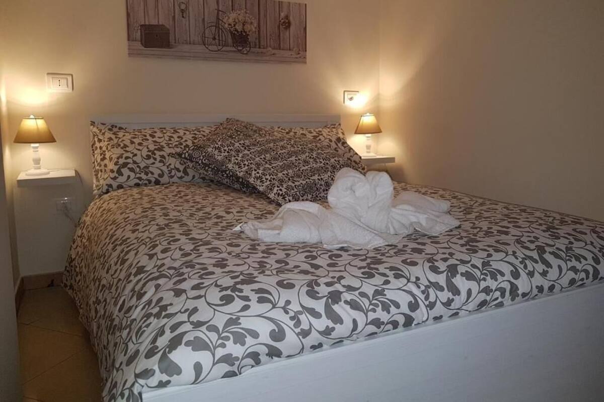 A neatly made bed with patterned bedding, two bedside lamps, and a wall-mounted artwork above the bed.