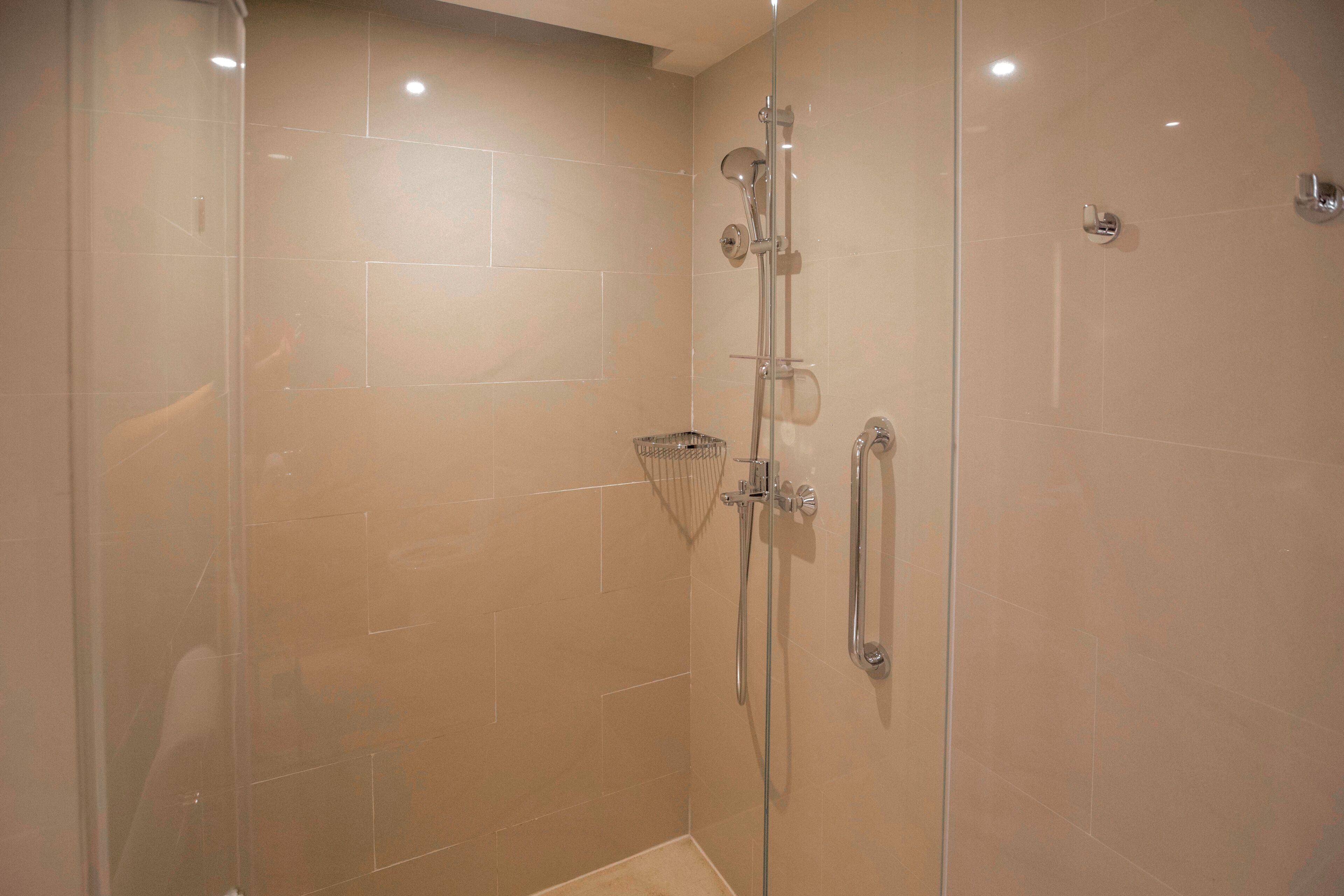 A glass-enclosed shower with a handheld showerhead and a wall-mounted faucet.