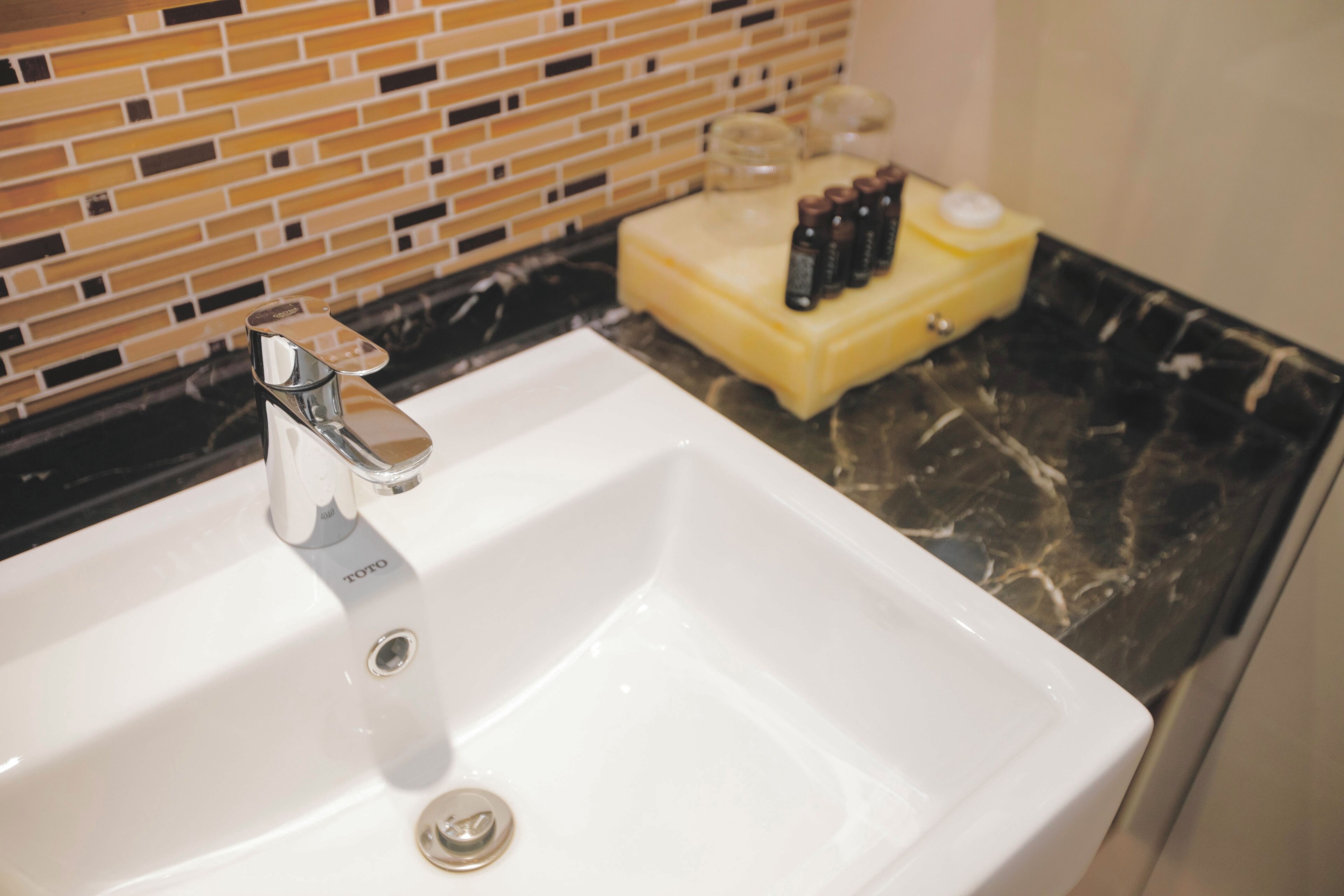 A white bathroom sink with a chrome faucet, a yellow soap dish, and a bottle of shampoo.