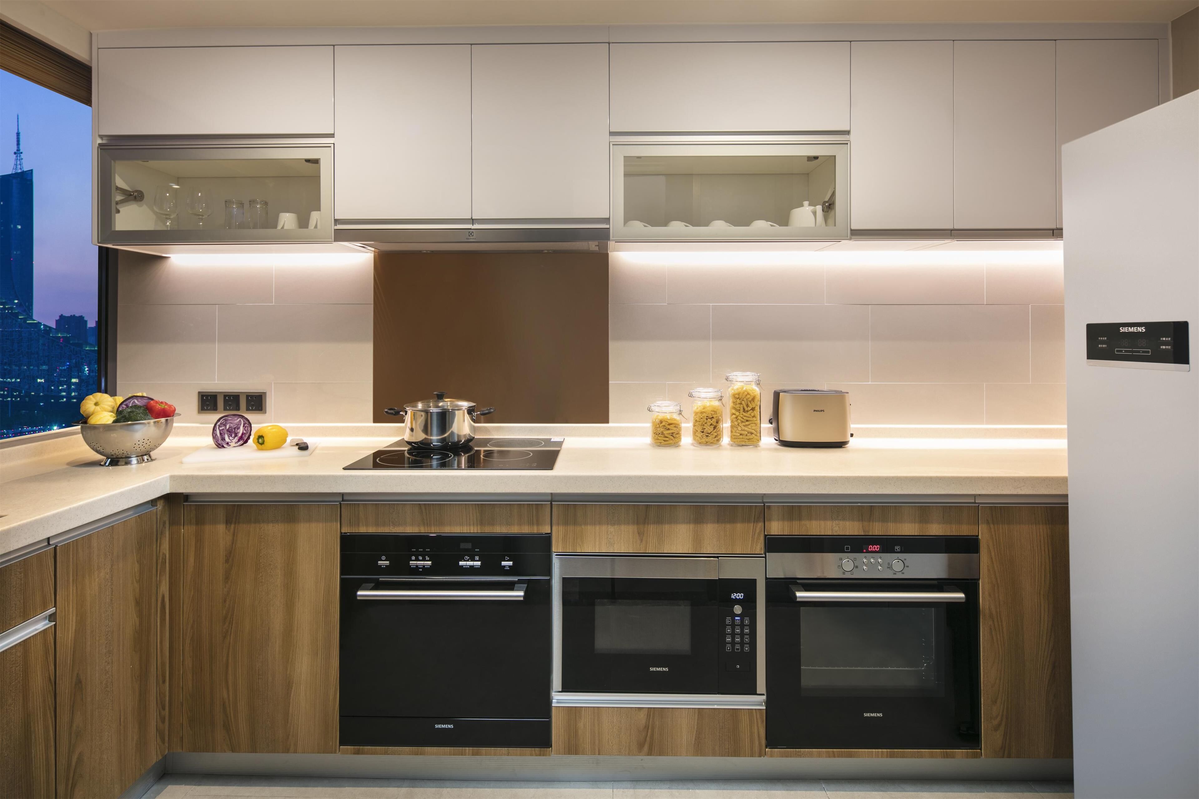 A modern kitchen with built-in appliances, including a dishwasher, oven, and microwave, with a city view through the window.