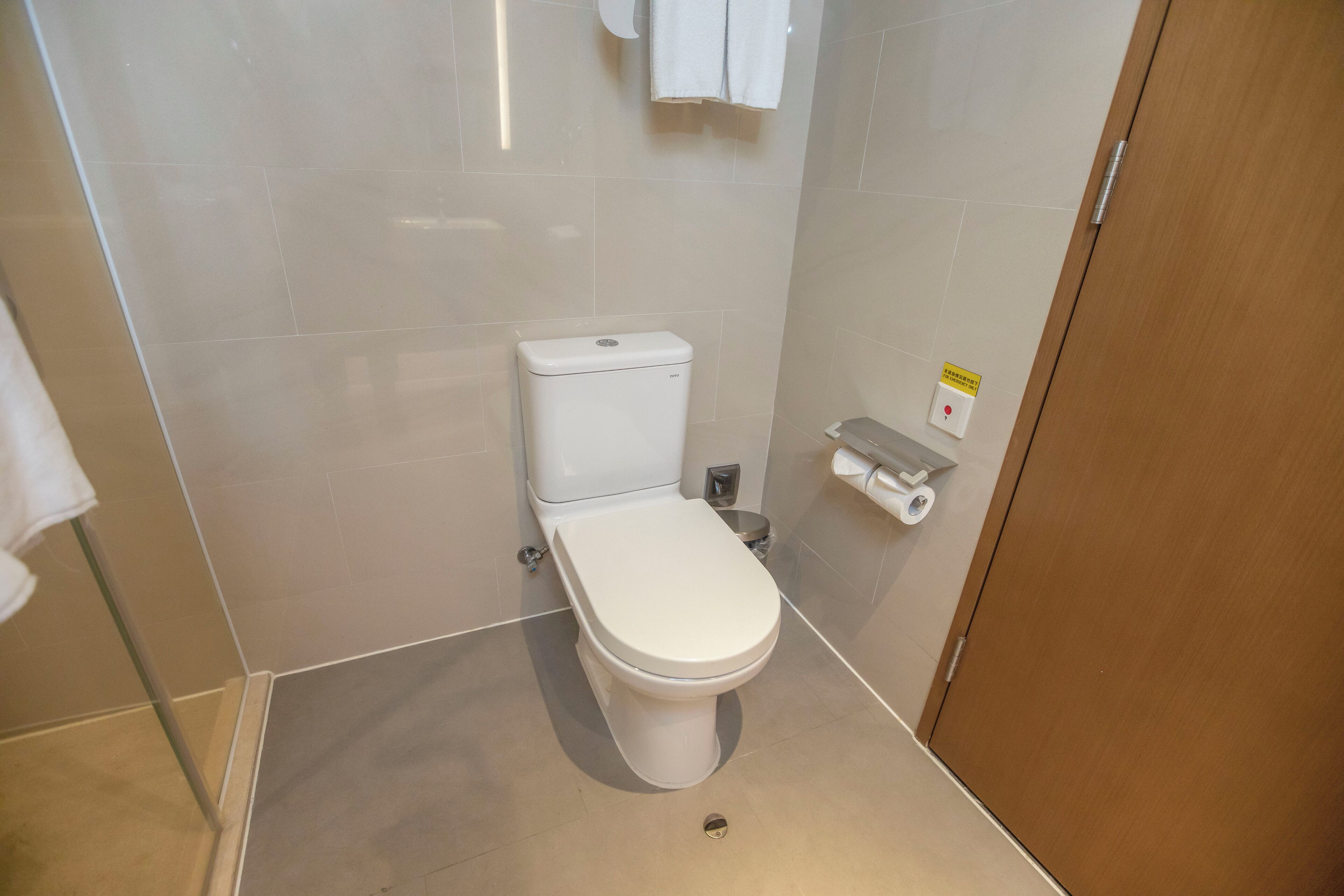 Une salle de bain moderne avec des toilettes blanches, une petite poubelle et un porte-rouleau de papier toilette fixé au mur.
