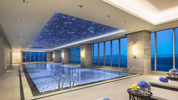 A modern indoor swimming pool with a starry ceiling, large windows, and a lounge area with towels and candles. - Somerset Swan Lake Hefei (Hefei)