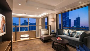 A modern hotel room with a balcony, a sofa, a coffee table, and a city view at dusk. - Somerset Swan Lake Hefei (Hefei)