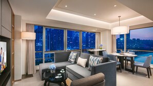 A modern living room with a large sofa, a coffee table, and a dining area with chairs. There are large windows with a city view. - Somerset Swan Lake Hefei (Hefei)