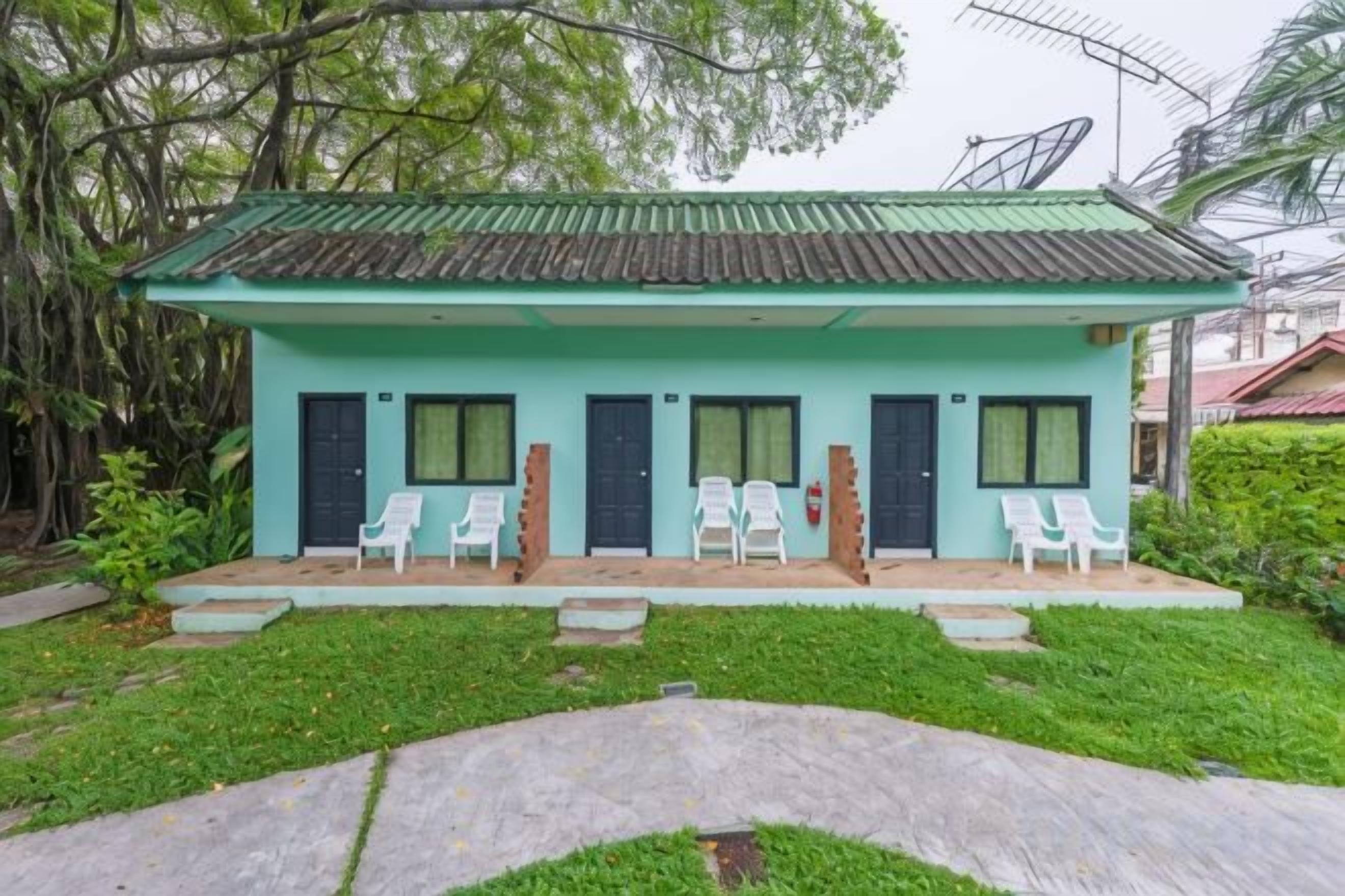 A small building with a green roof, four doors, and four white chairs outside.