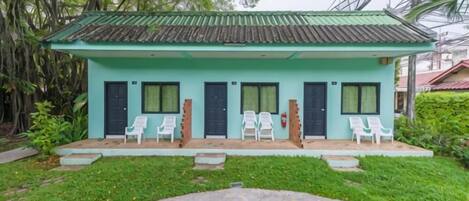 A small building with a green roof, four doors, and four white chairs outside.