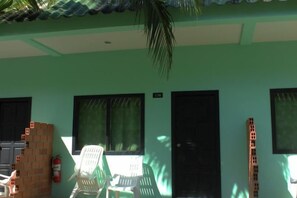 A building with a green exterior, black doors, and windows with curtains. There are white plastic chairs and a stack of bricks. - Baantonsai Garden Resort (Phuket)