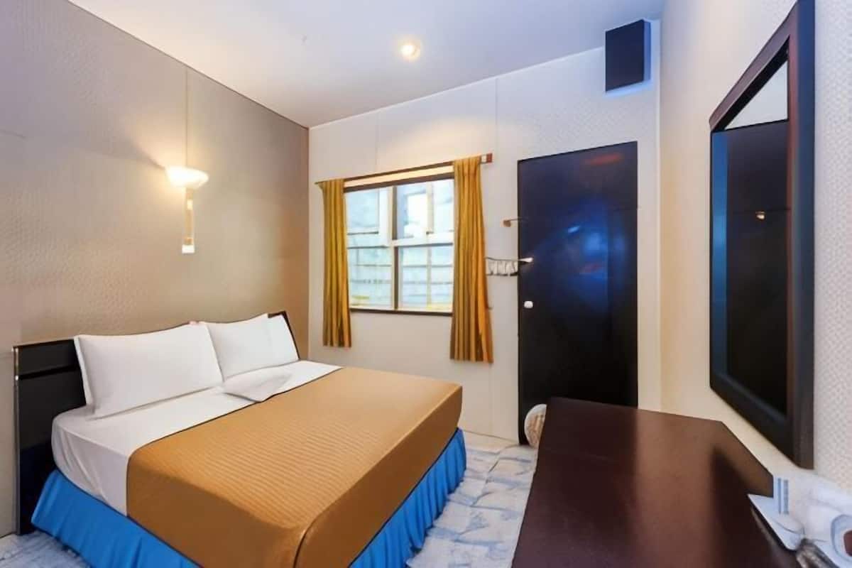 A hotel room with a bed, a desk, a window with curtains, and a door.