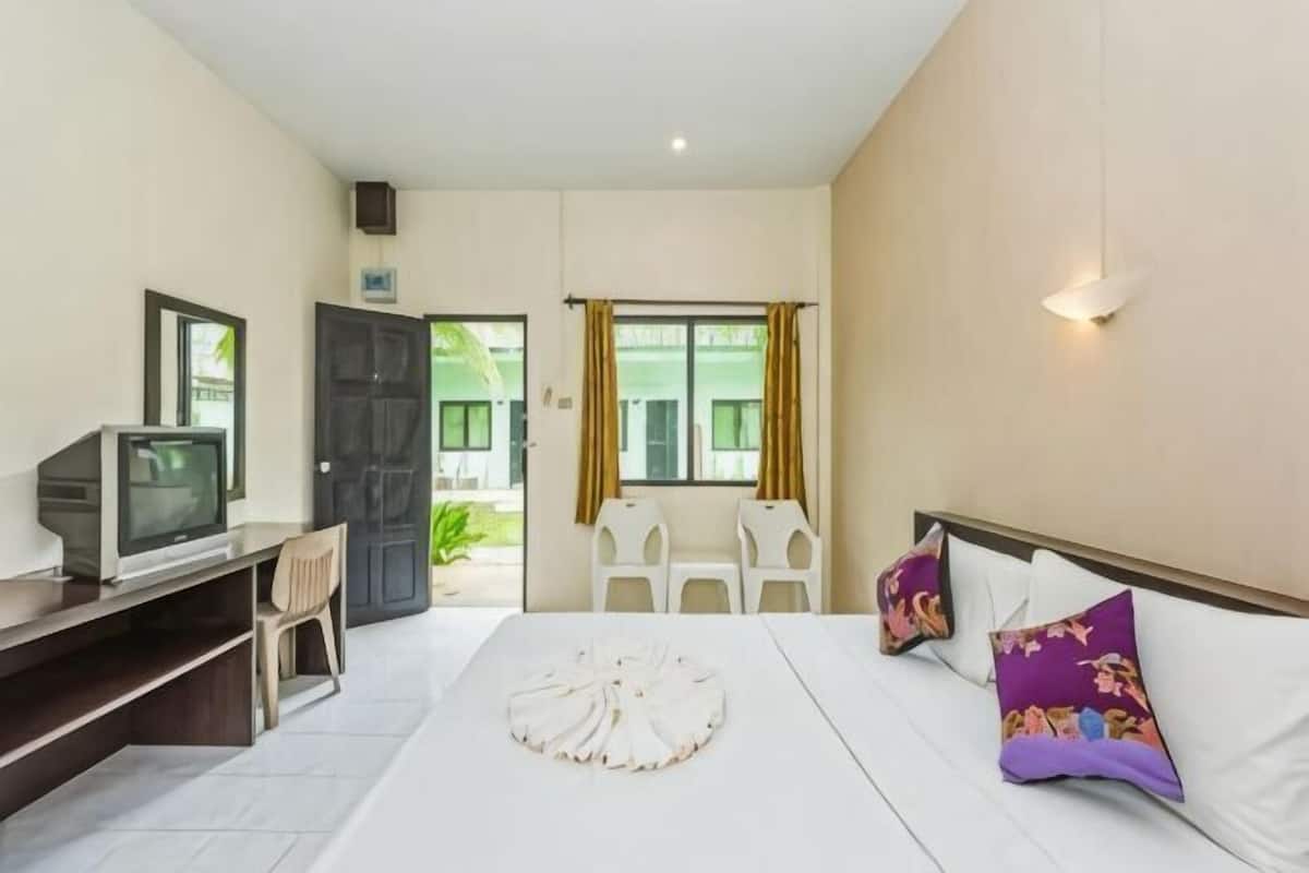 A hotel room with a bed, a desk with a television, a chair, and a window with curtains.