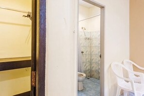 Un baño con inodoro, ducha y dos sillas de plástico blancas.