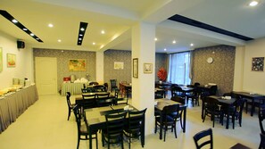 Comedor con varias mesas y sillas, una barra de buffet en un lateral y un amplio ventanal que proporciona luz natural.