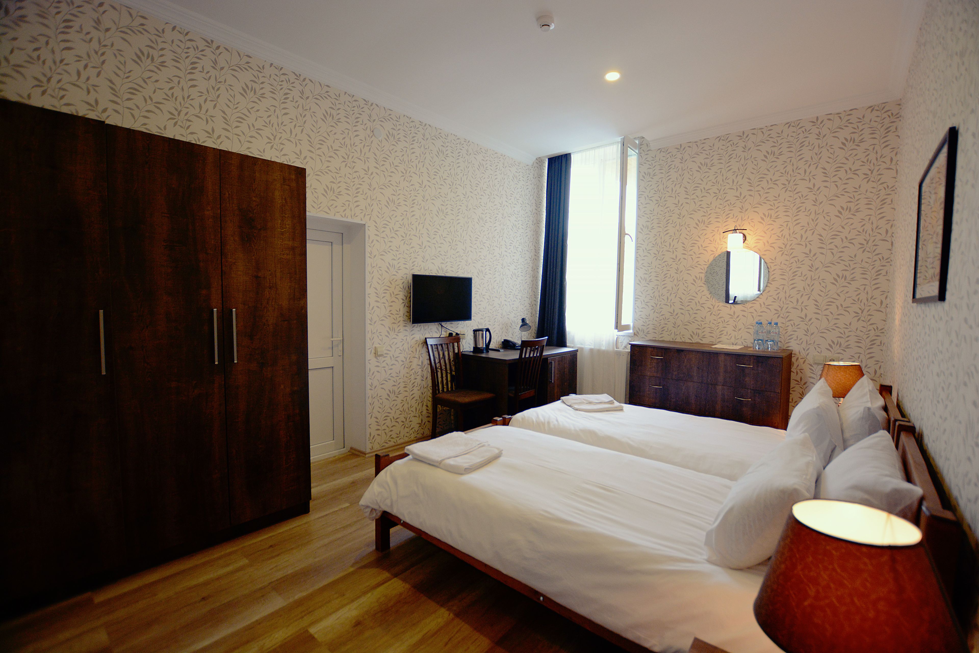 Ein Hotelzimmer mit einem großen Bett, einem Schreibtisch mit Stuhl, einem Kleiderschrank, einem Fernseher und einem Badezimmerspiegel.