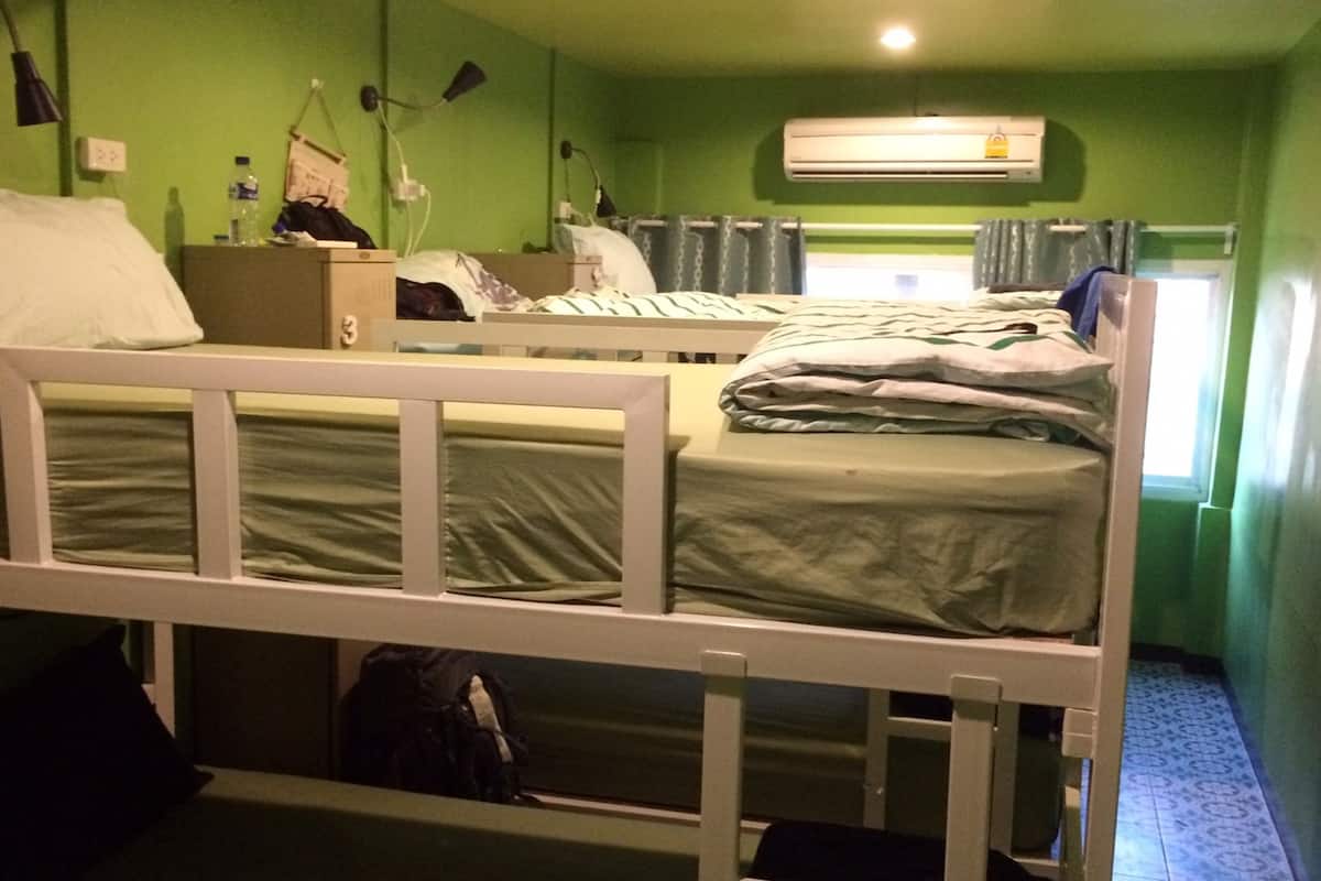 Una habitación con dos literas, una mesita de noche con lámpara, una botella de agua y una maleta.