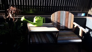 A wooden bench with a backrest and armrests, a small table, and a green watering can. - Staying Hostel (Bang Phli)