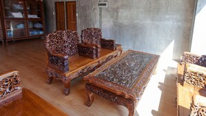 Una stanza con pavimento in legno, un tavolino da caffè in vetro e due sedie in legno decorate.