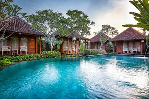 A poolside area with wooden bungalows, each with a chair and a small table. - Yana Villas Kemenuh by GenuineHost (Sukawati)