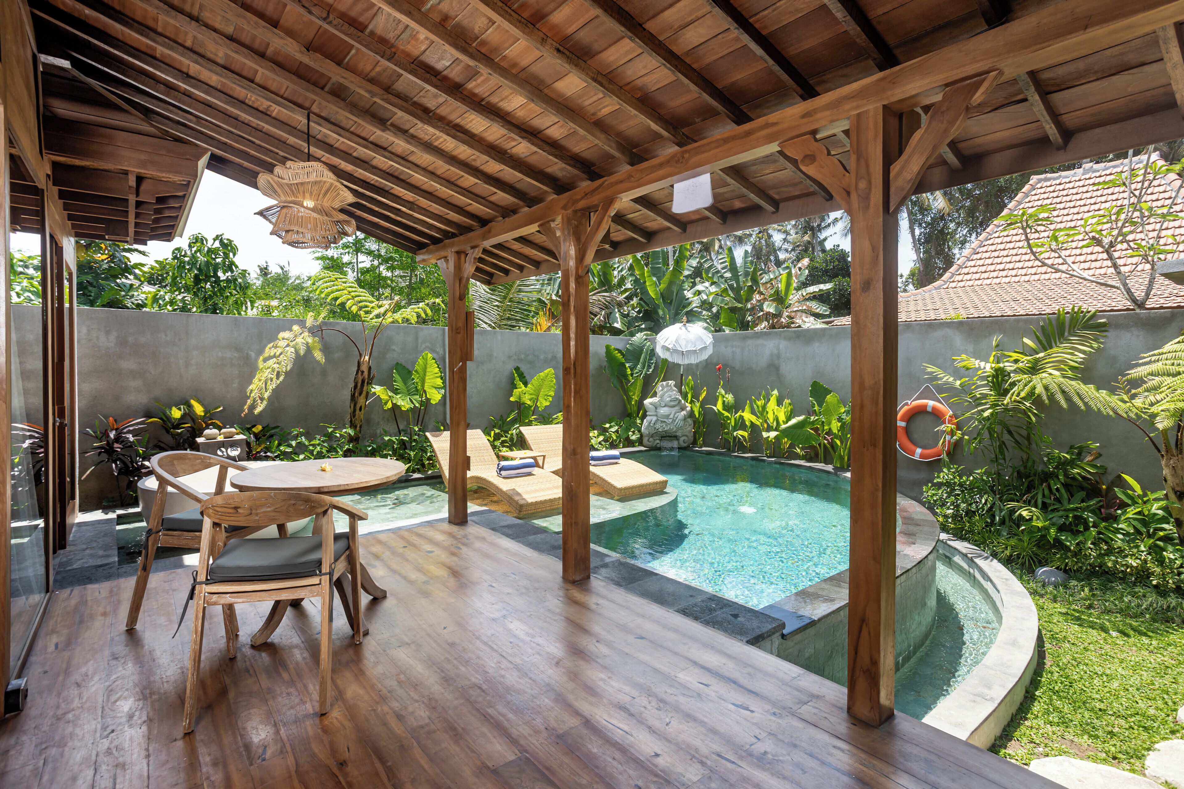A covered outdoor area with a pool, wooden furniture, and lush greenery.
