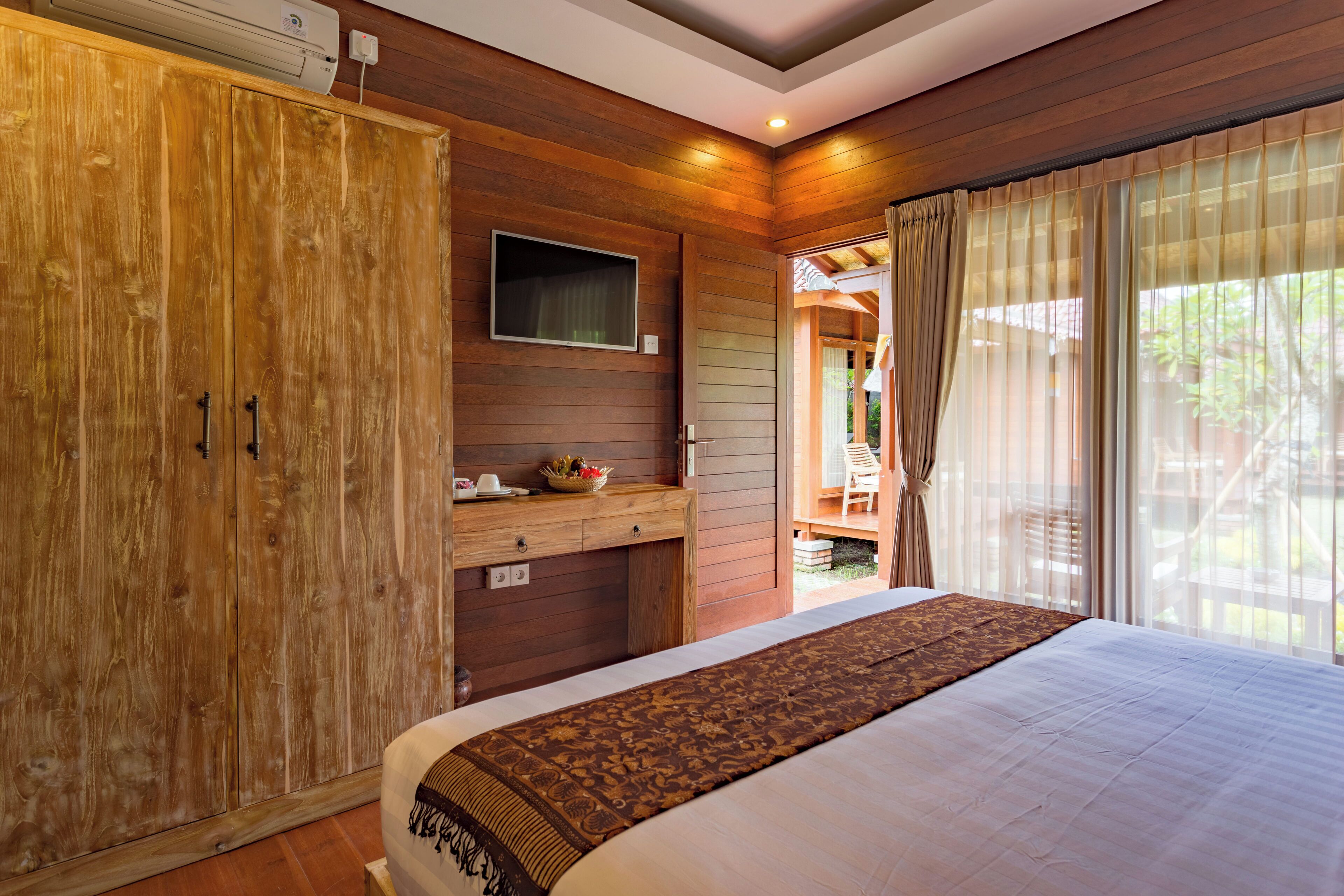 A bedroom with a large bed, wooden wardrobe, and a small desk with a television.