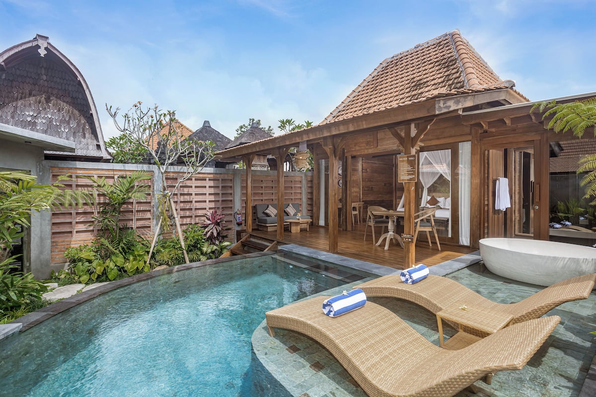 Una piscina con sillones de descanso, una terraza de madera y un área de estar techada.