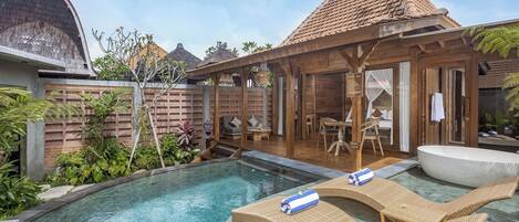 A pool with lounge chairs, a wooden deck, and a covered seating area.