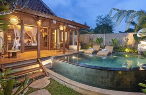 Una villa de madera con piscina, mobiliario de exterior y una zona cubierta con cama.
