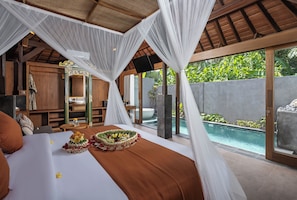 A bedroom with a large bed, a small table, a mirror, and a view of a swimming pool. - Yana Villas Kemenuh by GenuineHost (Sukawati)