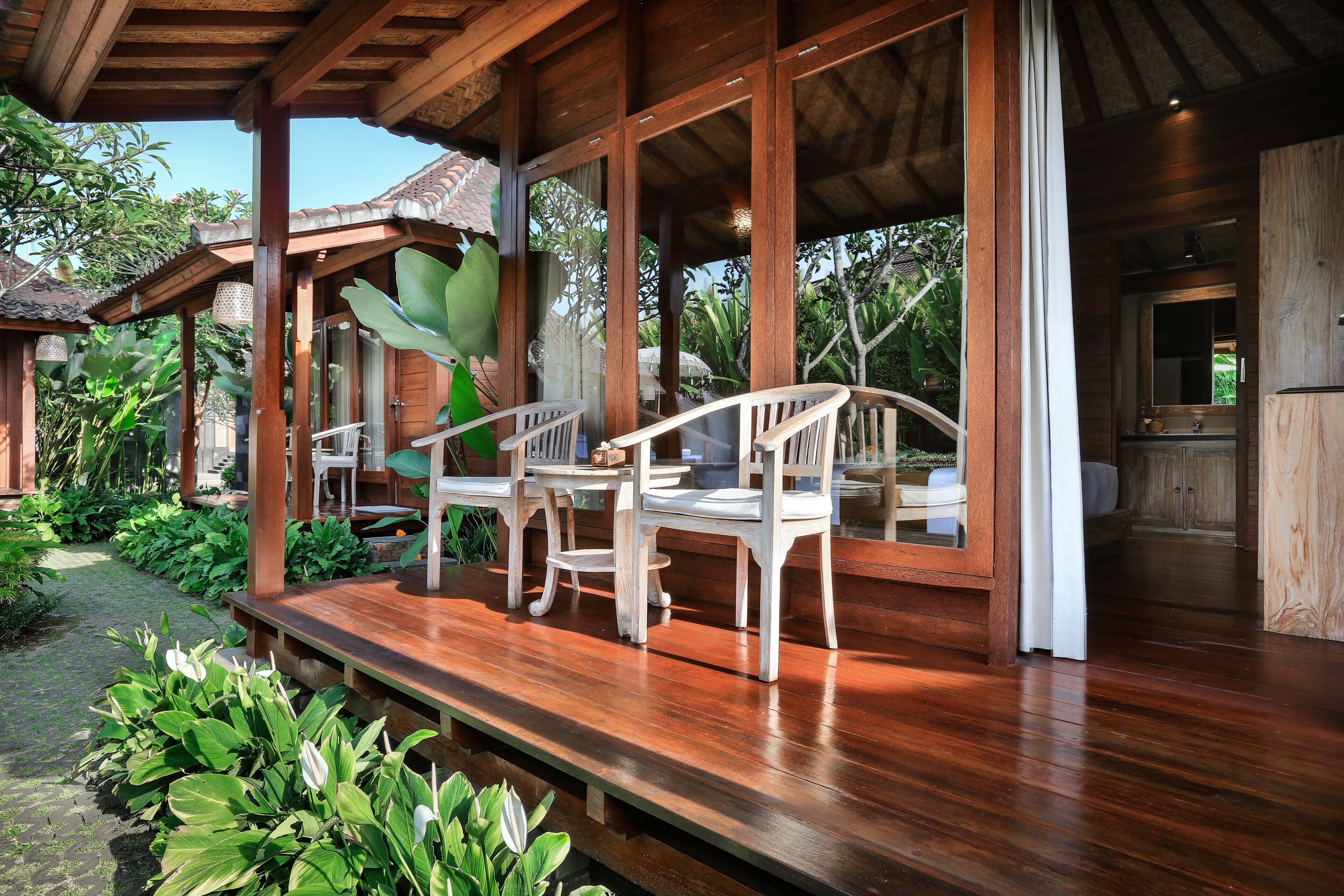 Une terrasse en bois, agrémentée de chaises blanches et d’une table, entourée d’une végétation luxuriante.