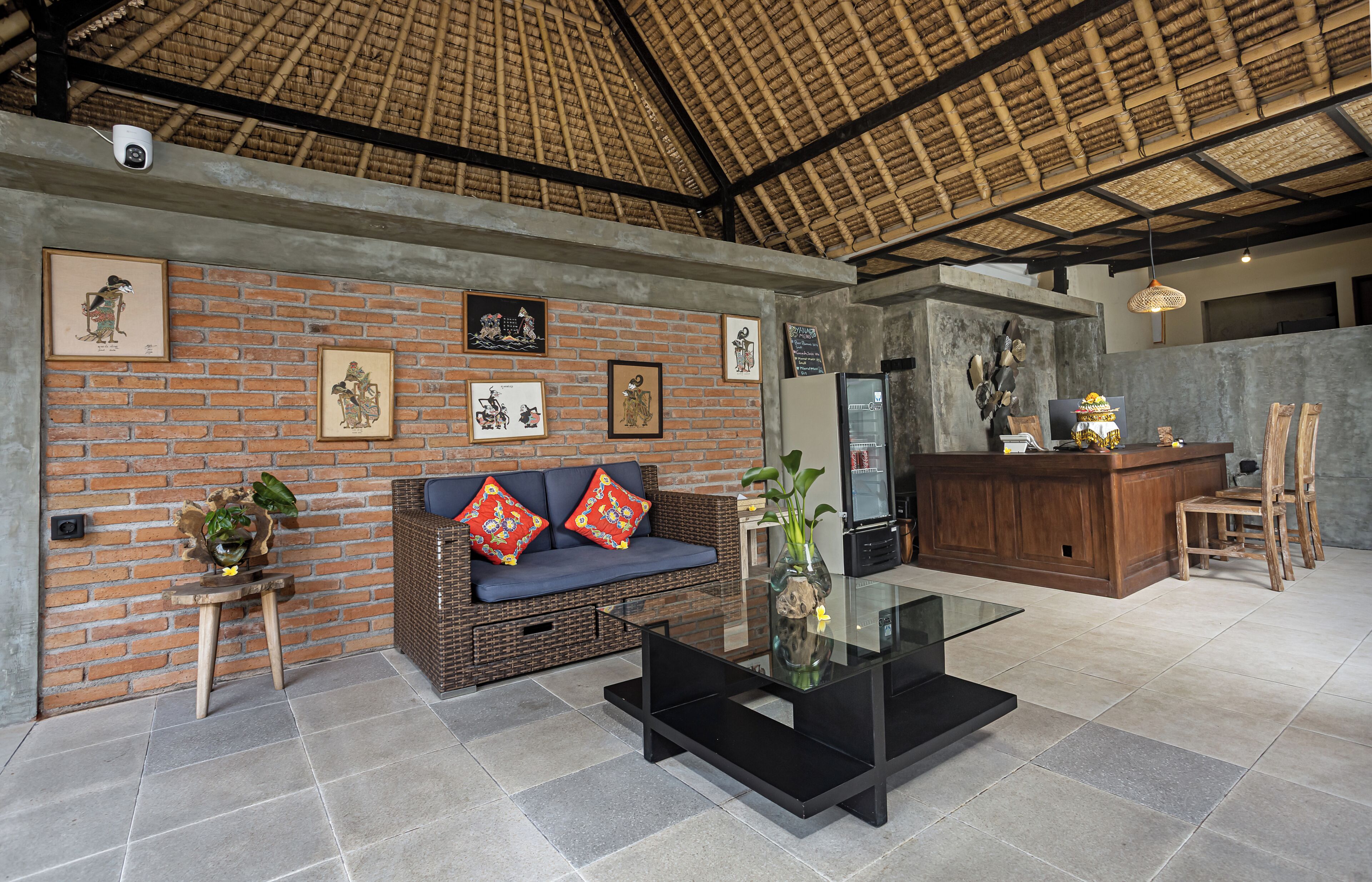 A modern interior with a brick wall, a sofa with colorful cushions, a glass coffee table, and a bamboo ceiling.