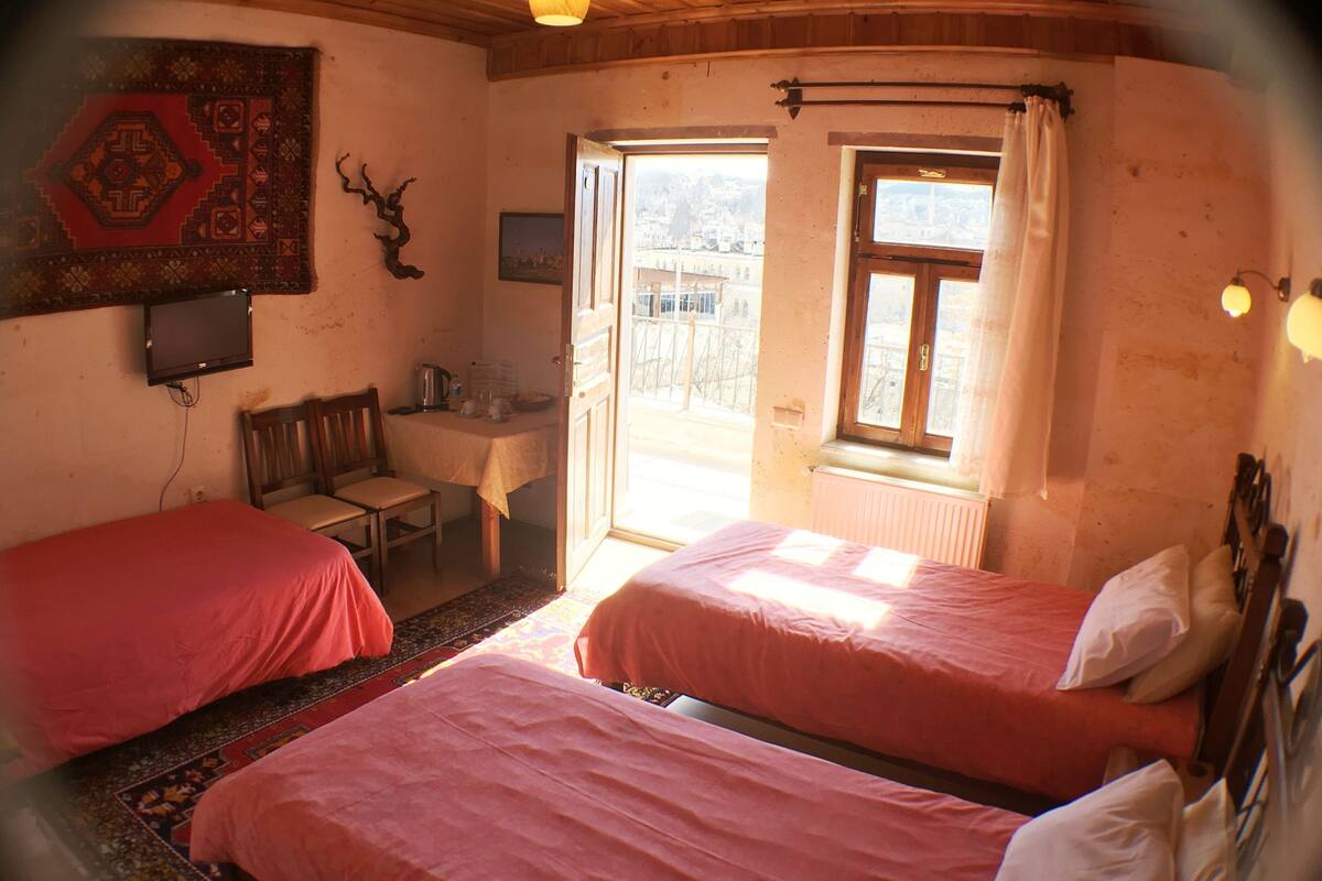 A room with two beds, a desk, a chair, a television, and a window with curtains.