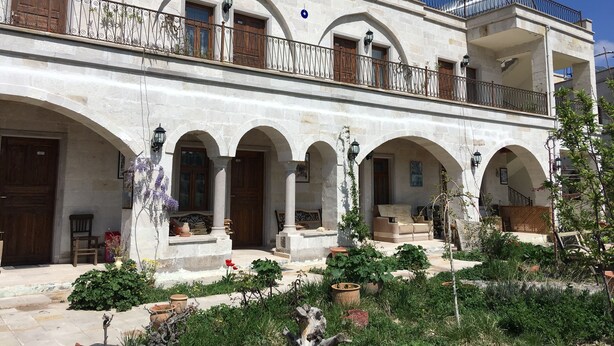 Un edificio a due piani con un cortile caratterizzato da archi, piante in vaso e mobili da esterno.