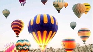 Un balcone con vista su un paesaggio montuoso e diversi palloni aerostatici colorati nel cielo.