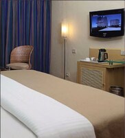 A hotel room with a bed, a chair, a television mounted on the wall, and a small table with a coffee maker.