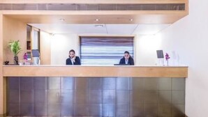 A reception desk with two staff members, a plant, and a small table with a vase. - The Royal Orchid (Mumbai)