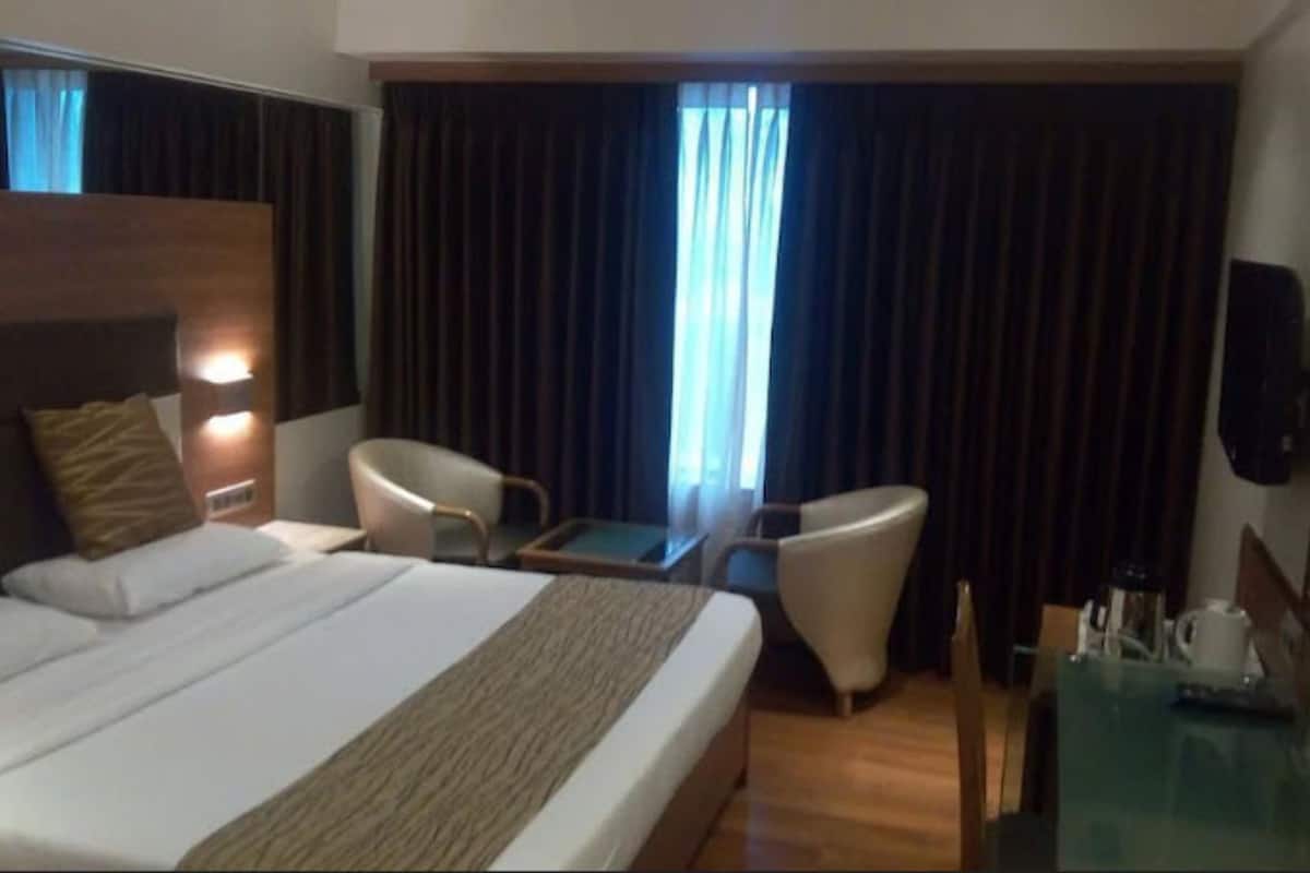 Une chambre d’hôtel avec un grand lit, deux fauteuils, une petite table et un téléviseur.